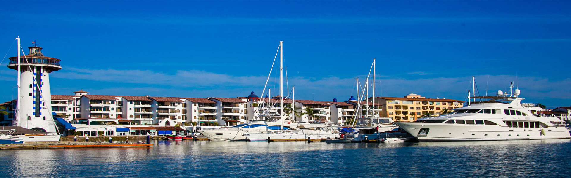 Picture of a beautiful harbor in Puerto Vallarta, Mexico.  The picture features blue water and white boats against a blue sky.